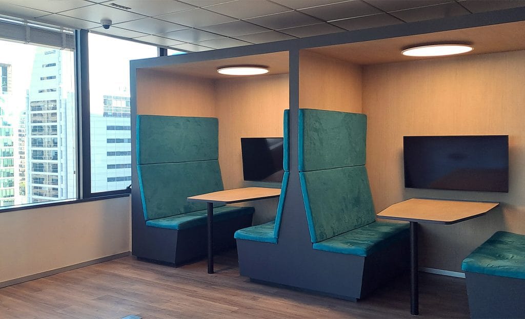 Nosotros 29 Oficina moderna con cabinas, asientos, mesas y pantallas. Ideal para trabajo colaborativo.